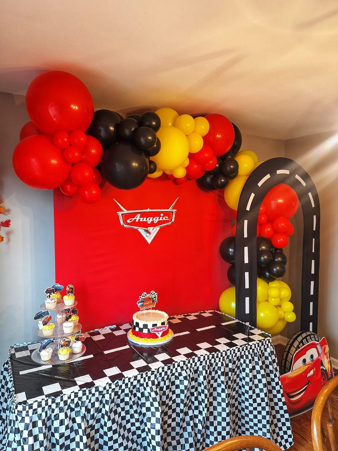 Cars-themed birthday party with red, black and yellow balloon garland, race track arch and checkered dessert table