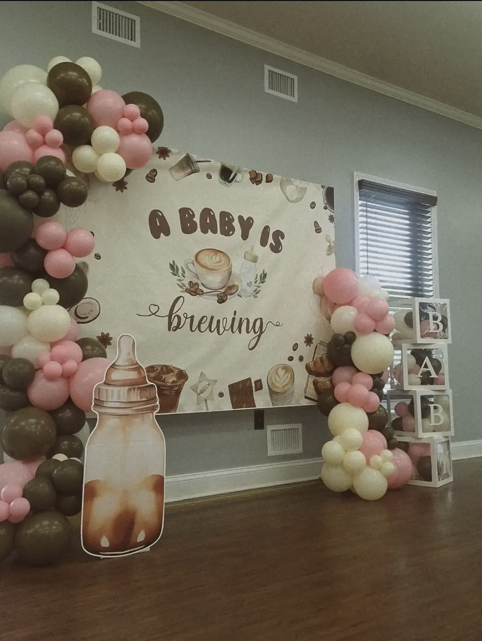 Coffee-themed baby shower backdrop with pink, cream and brown balloon garland and baby blocks